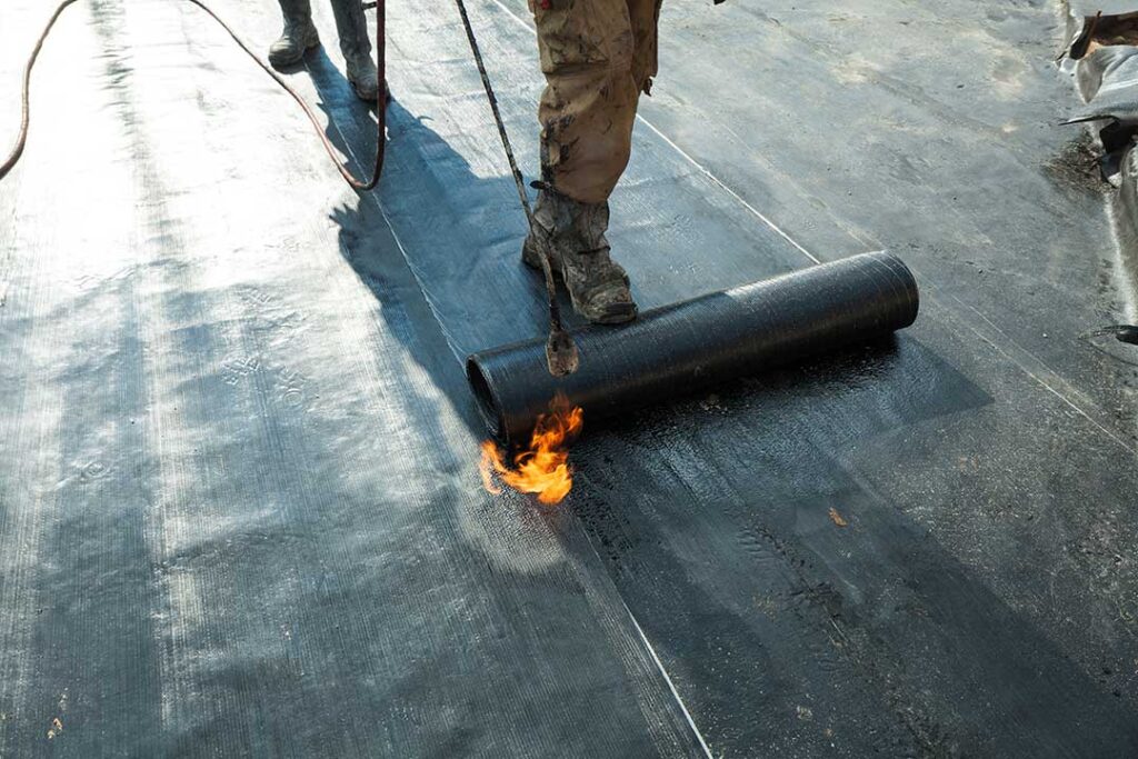 A person safely cleaning leaves out of a home gutter using gloves and a small scoop.