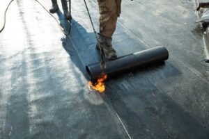 A person safely cleaning leaves out of a home gutter using gloves and a small scoop.