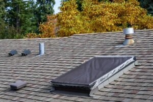 A homeowner examines curled and cracked asphalt shingles beside a ladder on a residential roof.